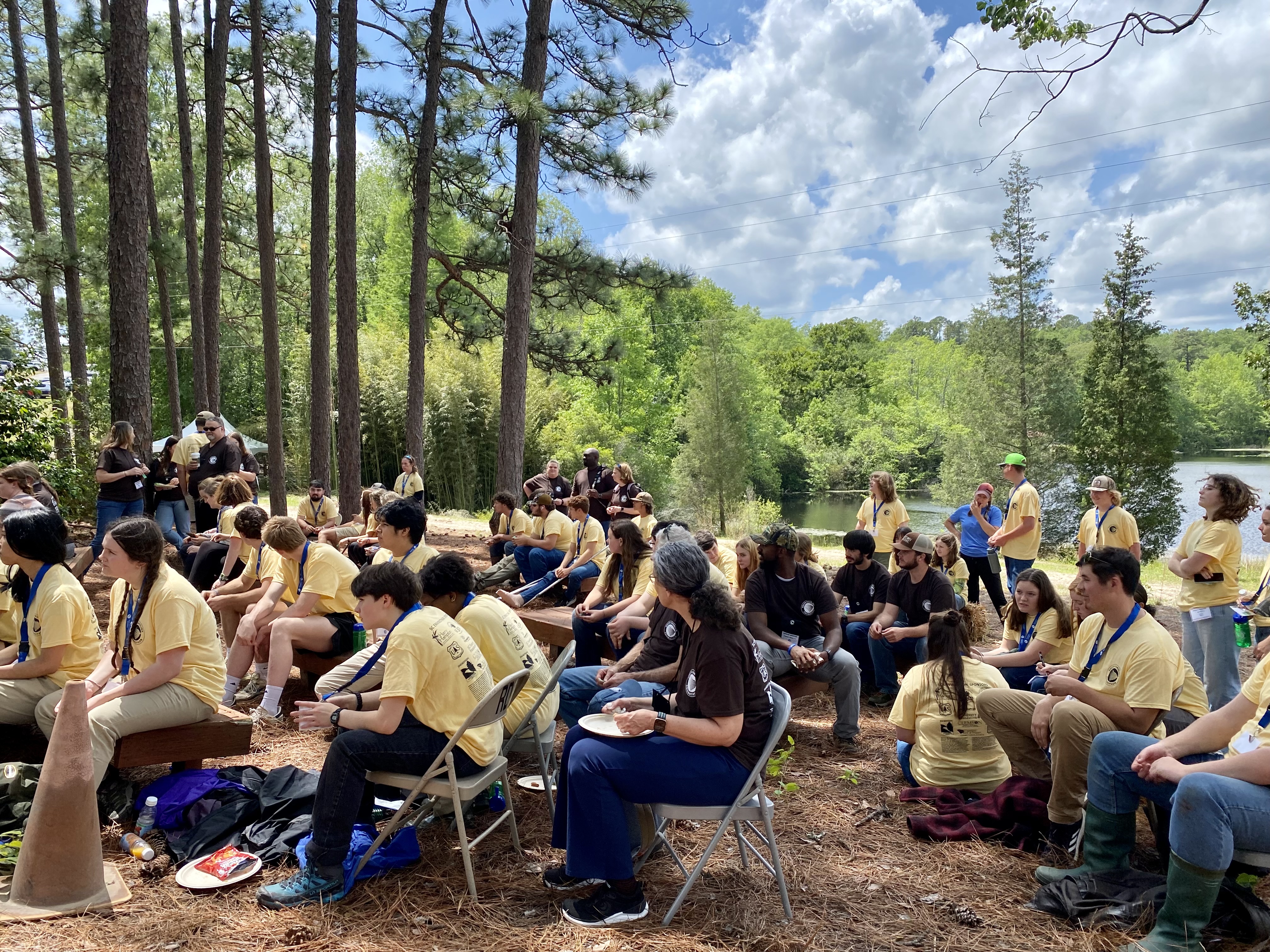 Students wearing matching yellow t-shirts sit in groups outdoors during the SC Envirothon competition